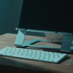 Notebook elevado em suporte de alumínio com teclado externo à frente sobre mesa de madeira